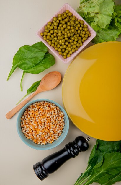 Draufsicht von getrockneten Maissamen mit Spinat-Salat der grünen Erbsen und leerem Teller auf Weiß
