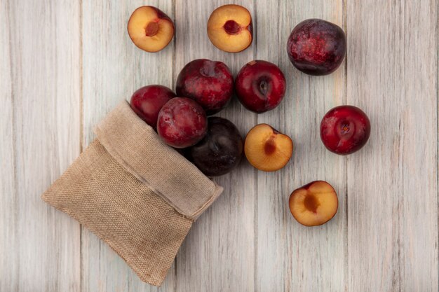 Draufsicht von glatthäutigen Pluots, die aus Sackleinenbeutel auf einer grauen Holzwand fallen