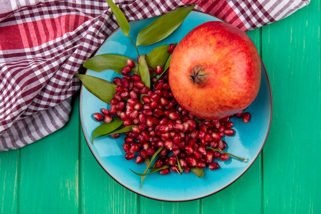 Draufsicht von Granatapfel und Granatapfelbeeren in Platte auf kariertem Stoff und grüner Oberfläche