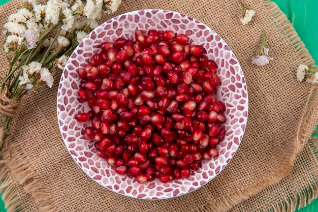 Draufsicht von Granatapfelbeeren mit Blumen auf Sackleinenoberfläche