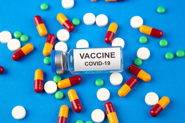 Draufsicht von grünen Medikamenten der weißen Pillen der weißen Kapseln und des Covid-Impfstoffs auf blauem Wellenhintergrund