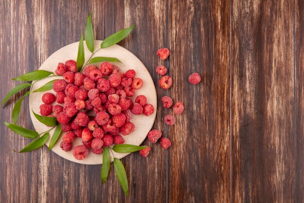 Draufsicht von Himbeeren auf Schneidebrett und Blättern auf Holzoberfläche