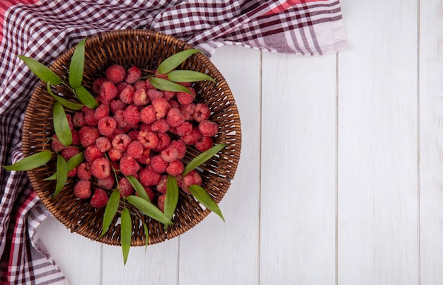 Draufsicht von Himbeeren und Blättern im Korb auf kariertem Stoff und Holzoberfläche