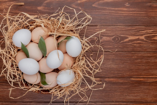 Draufsicht von Hühnereiern auf Nest mit Blättern auf einem hölzernen Hintergrund mit Kopienraum