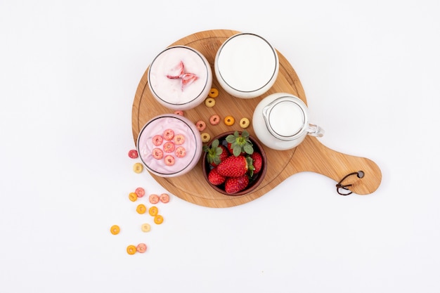 Draufsicht von Joghurt mit Milch und Erdbeere auf Holzschneidebrett auf weißer Fläche horizontal