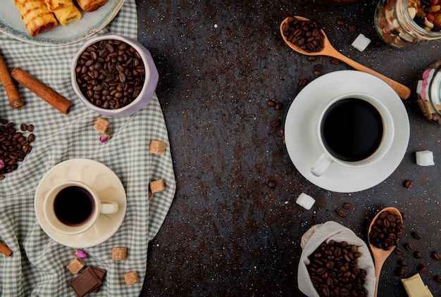 Draufsicht von Kaffeebohnen und Tassen Kaffee auf schwarzem Hintergrund mit Kopienraum