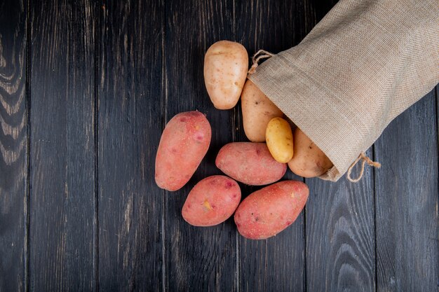 Draufsicht von Kartoffeln, die aus dem Sack auf Holzoberfläche mit Kopienraum verschüttet werden