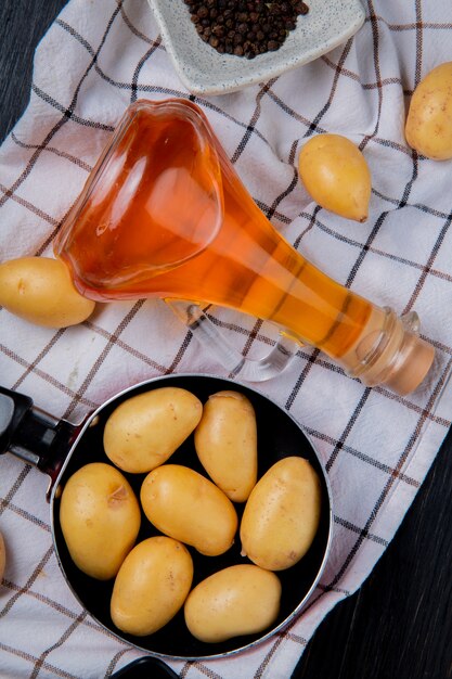 Draufsicht von Kartoffeln in der Pfanne und geschmolzener Butter mit schwarzen Pfeffersamen auf kariertem Stoff auf Holz