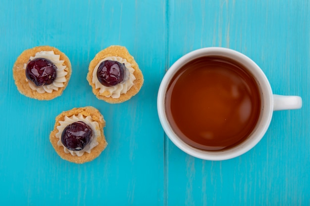 Draufsicht von kirschcupcakes und tasse tee auf blauem hintergrund