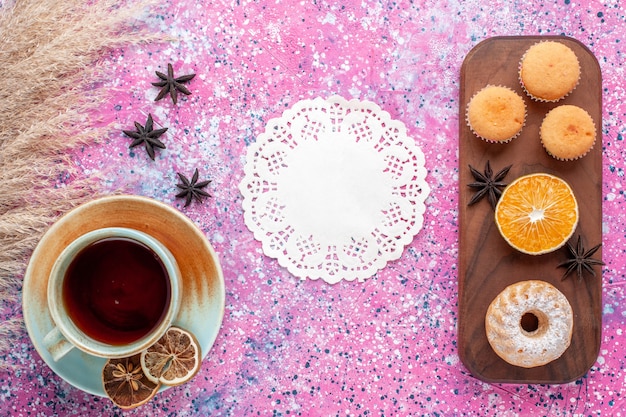 Draufsicht von kleinen Kuchen mit Orangenscheibe und Tasse Tee auf der hellrosa Oberfläche