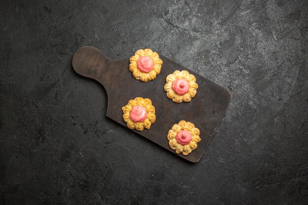 Draufsicht von kleinen Zuckerkeksen mit Erdbeercreme auf der grauen Oberfläche