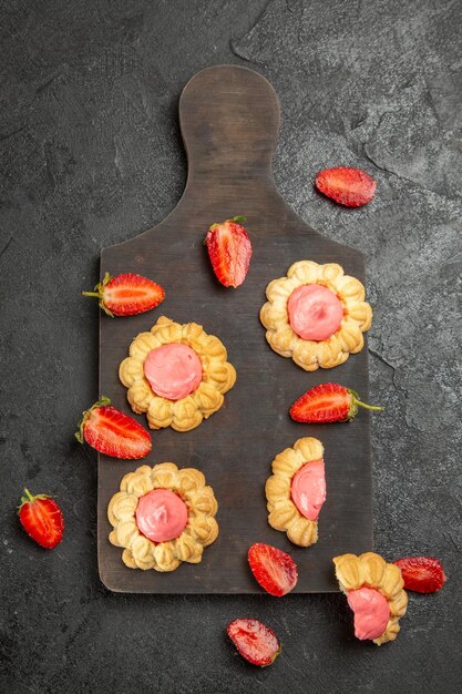 Draufsicht von kleinen Zuckerkeksen mit Erdbeercreme auf der grauen Oberfläche