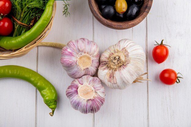 Draufsicht von Knoblauchknollen mit Oliven, Pfeffer und Kirschtomaten auf Holzoberfläche