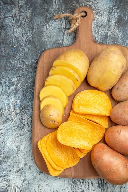 Draufsicht von knusprigen Pommes und ungekochten Kartoffeln auf hölzernem Schneidebrett auf grauem Tisch