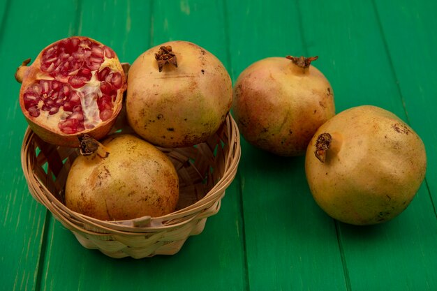 Draufsicht von köstlichen frischen Granatäpfeln auf einem Eimer mit Granatäpfeln lokalisiert auf einer grünen Holzoberfläche