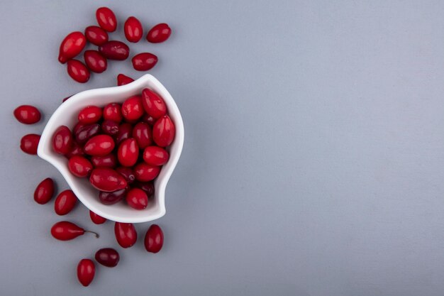 Draufsicht von Kornelkirschenbeeren in der Schüssel und auf grauem Hintergrund mit Kopienraum