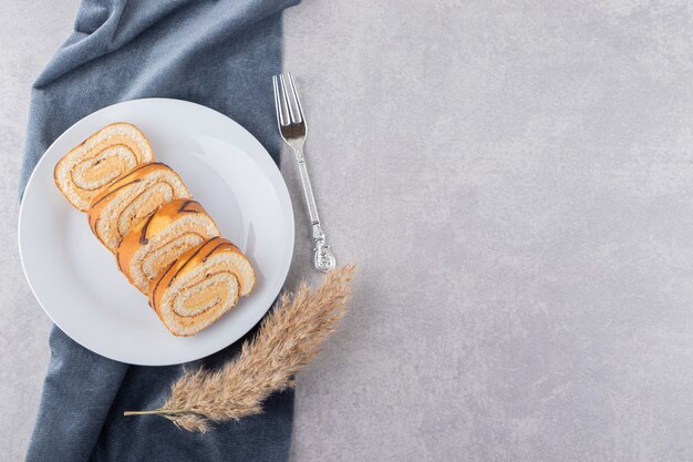 Draufsicht von Kuchenrollen auf weißem Teller über grauem Hintergrund.