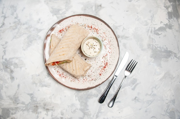 Kostenloses Foto draufsicht von lavash wrap und joghurt in einer kleinen schüssel auf einem teller und besteck auf befleckter weißer oberfläche