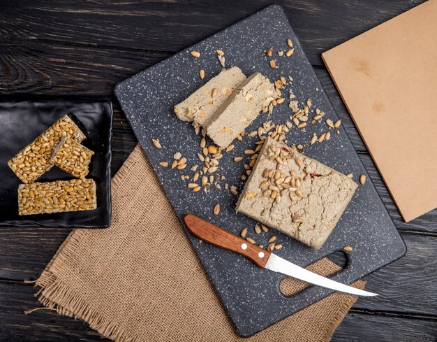 Draufsicht von leckeren Halva-Scheiben mit Sonnenblumenkernen auf einem schwarzen Schneidebrett