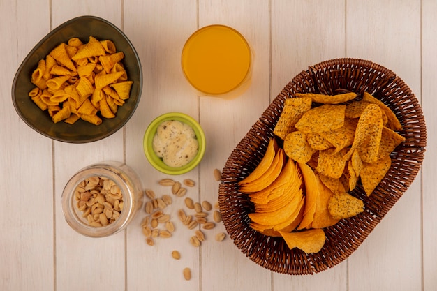 Draufsicht von leckeren knusprigen Pommes auf einem Eimer mit einem Glas Orangensaft mit Soße mit Pinienkernen auf einem Glas auf einem beigen Holztisch