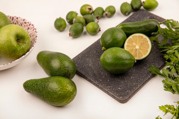 Draufsicht von Limetten auf einem Küchenbrett mit Gurkenfeijoas und Avocados lokalisiert auf einer weißen Wand