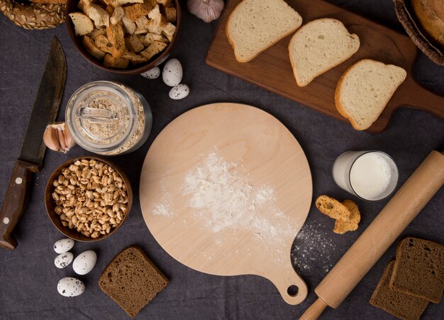 Draufsicht von Nahrungsmitteln als Mehl Haferflocken Hühneraugen Eier mit Brot Messer Schneidebrett Milch auf kastanienbraunem Hintergrund