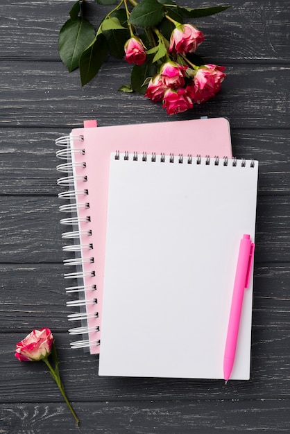 Draufsicht von Notizbüchern auf hölzernem Schreibtisch mit Blumenstrauß von Rosen
