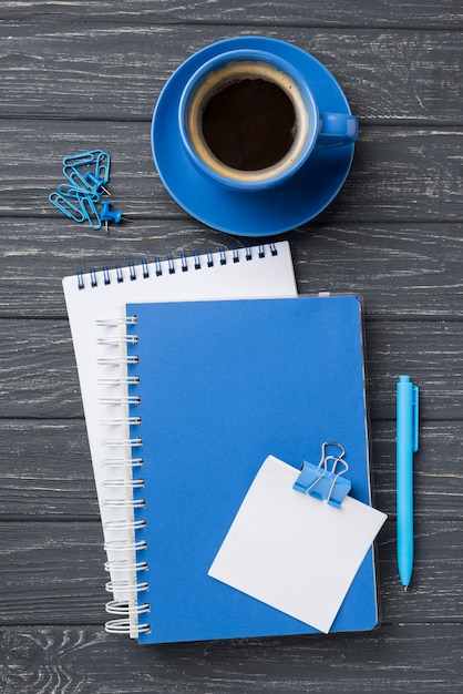 Draufsicht von Notizbüchern auf hölzernem Schreibtisch mit Kaffeetasse und Stift