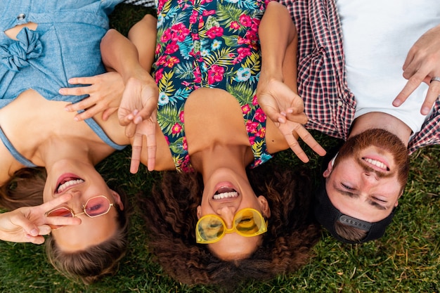 Draufsicht von oben auf bunte stilvolle glückliche junge Gesellschaft von Freunden, die auf Gras im Park liegen, Mann und Frauen, die Spaß zusammen haben