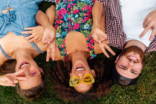 Draufsicht von oben auf bunte stilvolle glückliche junge Gesellschaft von Freunden, die auf Gras im Park liegen, Mann und Frauen, die Spaß zusammen haben