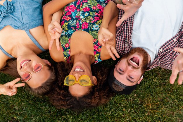 Draufsicht von oben auf bunte stilvolle glückliche junge Gesellschaft von Freunden, die auf Gras im Park liegen, Mann und Frauen, die Spaß zusammen haben