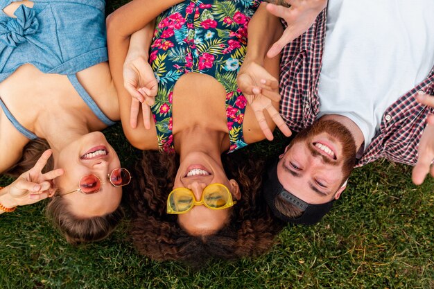 Draufsicht von oben auf bunte stilvolle glückliche junge Gesellschaft von Freunden, die auf Gras im Park liegen, Mann und Frauen, die Spaß zusammen haben