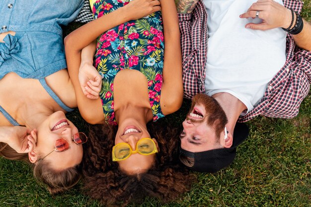 Draufsicht von oben auf bunte stilvolle glückliche junge Gesellschaft von Freunden, die auf Gras im Park liegen, Mann und Frauen, die Spaß zusammen haben