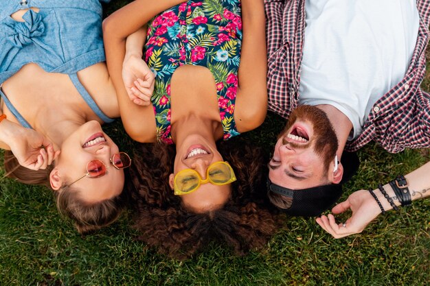 Draufsicht von oben auf bunte stilvolle glückliche junge Gesellschaft von Freunden, die auf Gras im Park liegen, Mann und Frauen, die Spaß zusammen haben