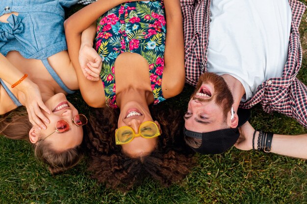 Draufsicht von oben auf bunte stilvolle glückliche junge Gesellschaft von Freunden, die auf Gras im Park liegen, Mann und Frauen, die Spaß zusammen haben