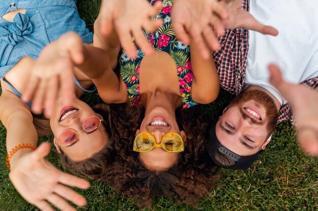 Draufsicht von oben auf bunte stilvolle glückliche junge Gesellschaft von Freunden, die auf Gras im Park liegen, Mann und Frauen, die Spaß zusammen haben