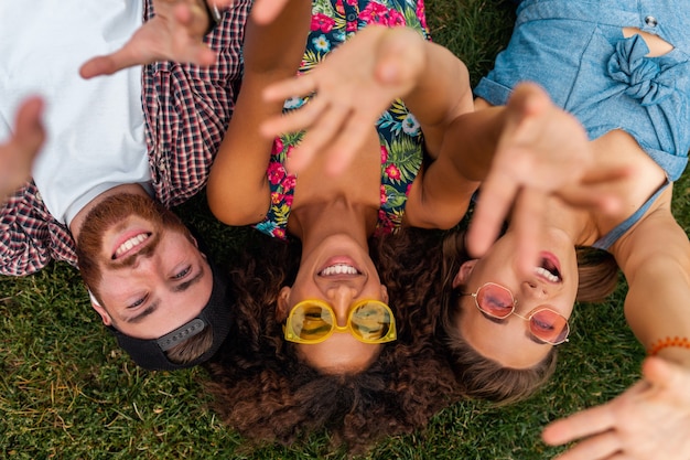 Draufsicht von oben auf bunte stilvolle glückliche junge Gesellschaft von Freunden, die auf Gras im Park liegen, Mann und Frauen, die Spaß zusammen haben