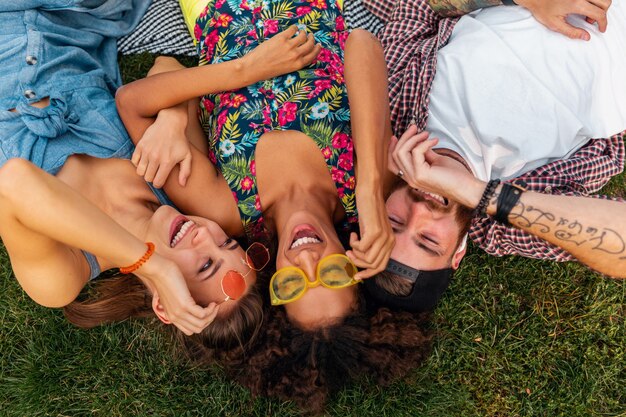 Draufsicht von oben auf bunte stilvolle glückliche junge Gesellschaft von Freunden, die auf Gras im Park liegen, Mann und Frauen, die Spaß zusammen haben