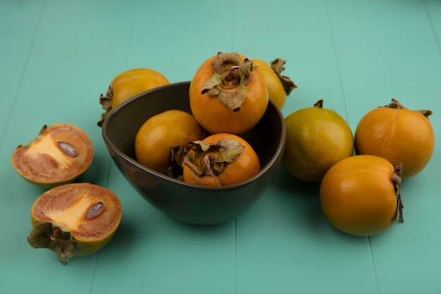 Kostenloses Foto draufsicht von orange unreifen persimonenfrüchten auf einer schüssel mit persimonenfrüchten lokalisiert auf einem blauen holztisch