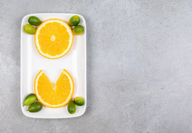 Draufsicht von Orangenscheiben mit Kumquats auf weißem Teller.