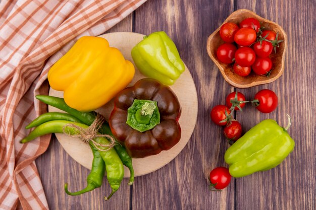 Draufsicht von Paprika auf Schneidebrett mit Schüssel Tomate und kariertem Stoff auf Holzoberfläche