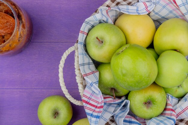 Draufsicht von Äpfeln im Korb mit Apfelmarmelade auf lila Hintergrund