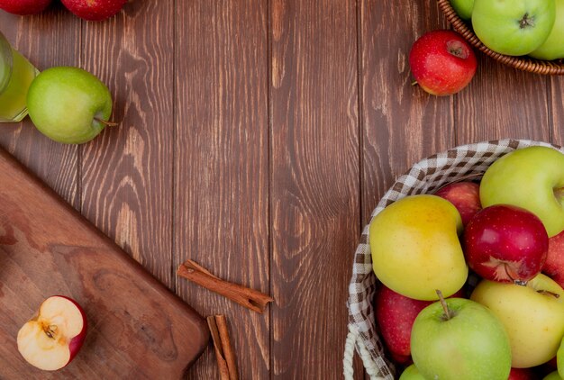 Draufsicht von Äpfeln in Körben und auf Schneidebrett mit Zimtapfelsaft auf hölzernem Hintergrund