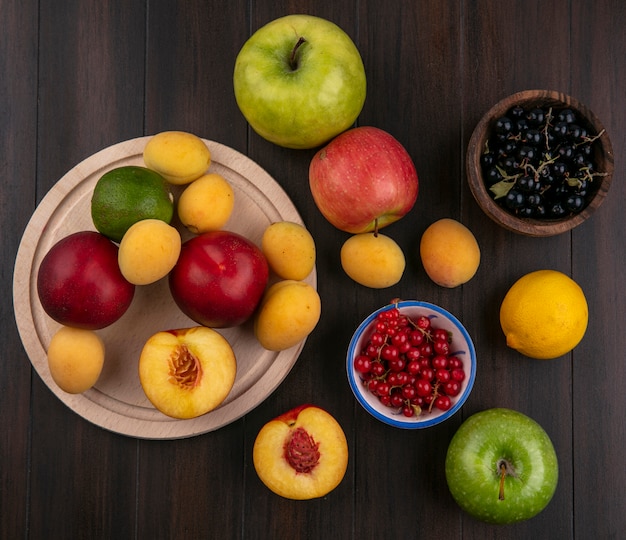 Draufsicht von Pfirsichen auf einem Stand mit Aprikosenäpfeln und roten und schwarzen Johannisbeeren auf einer Holzoberfläche