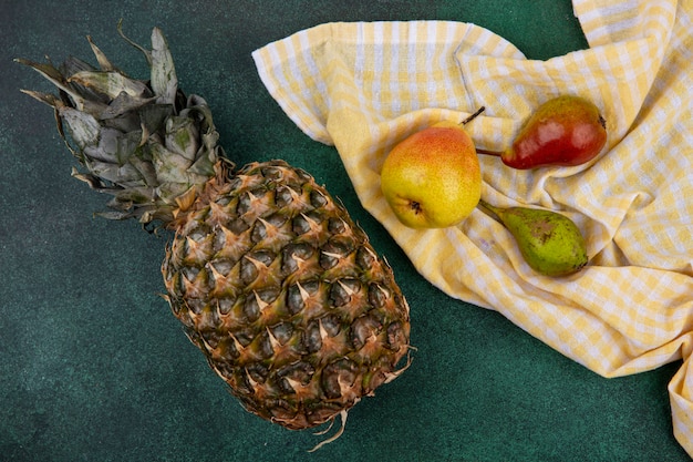 Draufsicht von Pfirsichen auf kariertem Stoff mit Ananas auf grüner Oberfläche