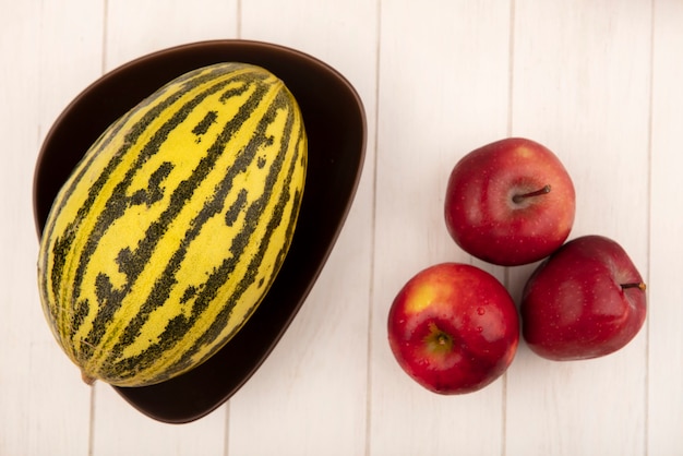 Draufsicht von reifen roten Äpfeln mit Melone Melone auf einer Schüssel auf einer weißen Holzoberfläche