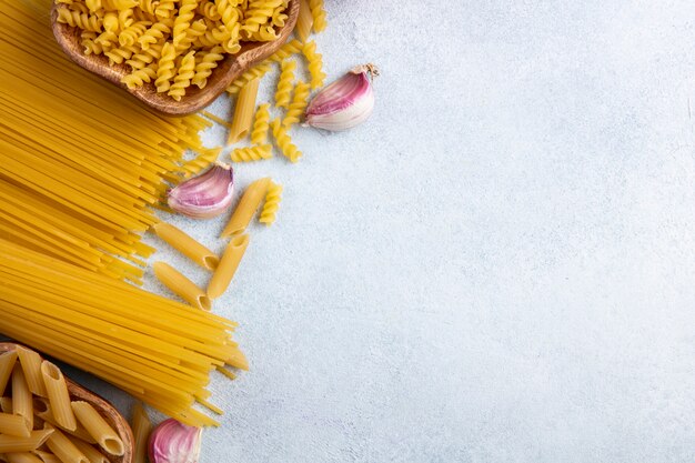 Draufsicht von rohen Spaghetti mit rohen Nudeln in Schalen mit Knoblauch auf einer grauen Oberfläche