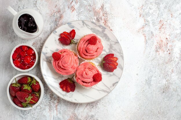 Draufsicht von rosa Erdbeerkuchen mit Marmelade und Schokoriegeln auf weißer Oberfläche