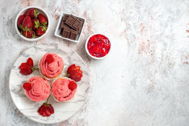 Draufsicht von rosa Erdbeerkuchen mit Marmelade und Schokoriegeln auf weißer Oberfläche