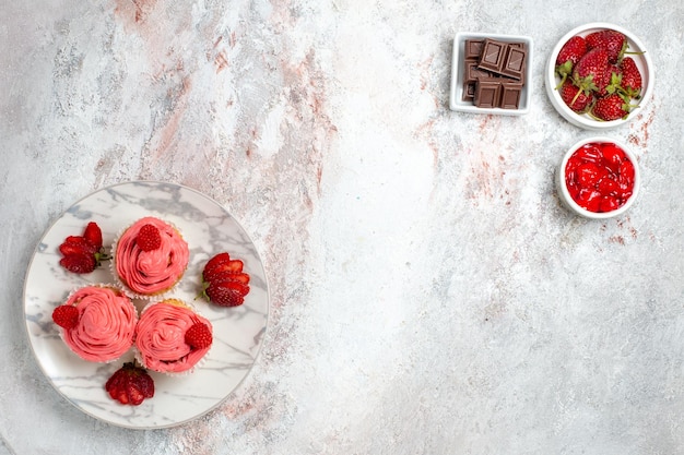 Draufsicht von rosa Erdbeerkuchen mit Marmelade und Schokoriegeln auf weißer Oberfläche